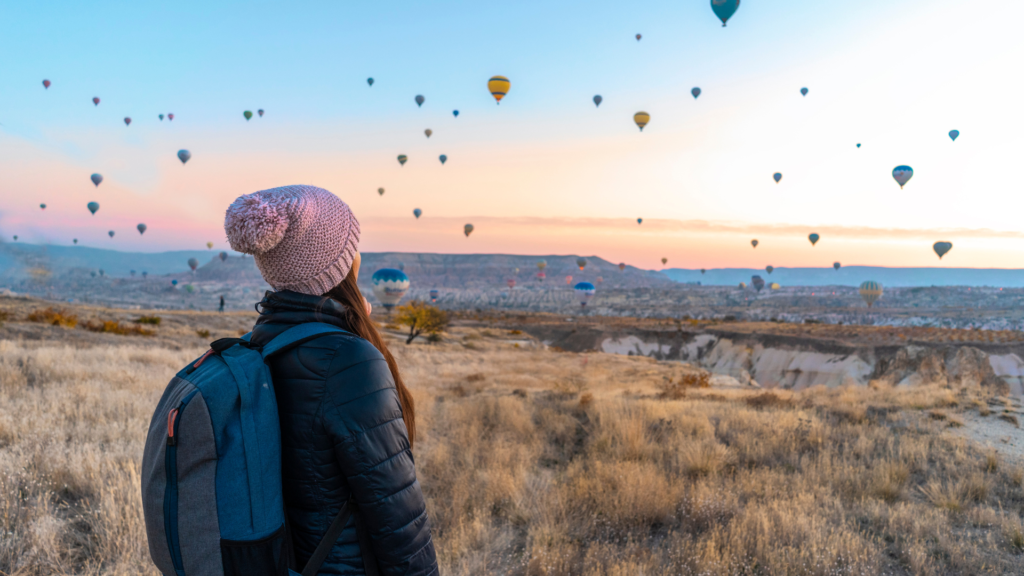 woman looking at a lot of hot air balloons inthe sky
