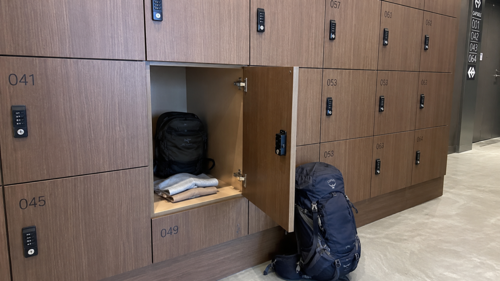 Open luggage locker at a capsule hotel with a small bag inside and a large backpack that won't fit