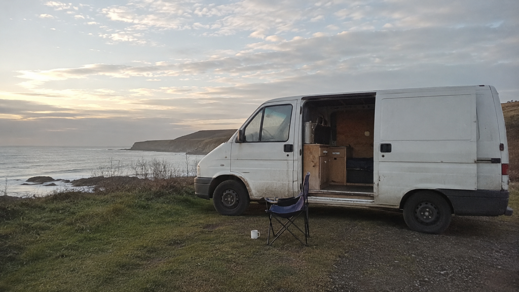 Budget van life setup — a simple converted panel van parked at a coastal layby with the side door open