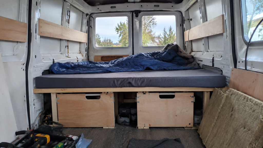 DIY budget camper van conversion interior with plywood bed platform and under-bed storage