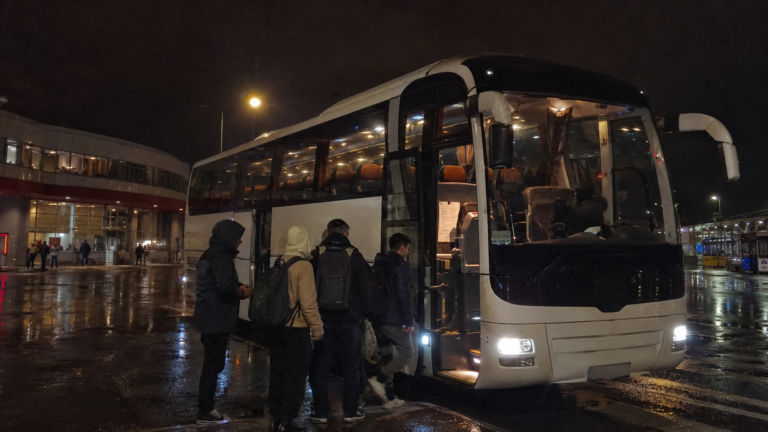 Travellers with backpacks boarding a long-distance night bus at a dimly lit station