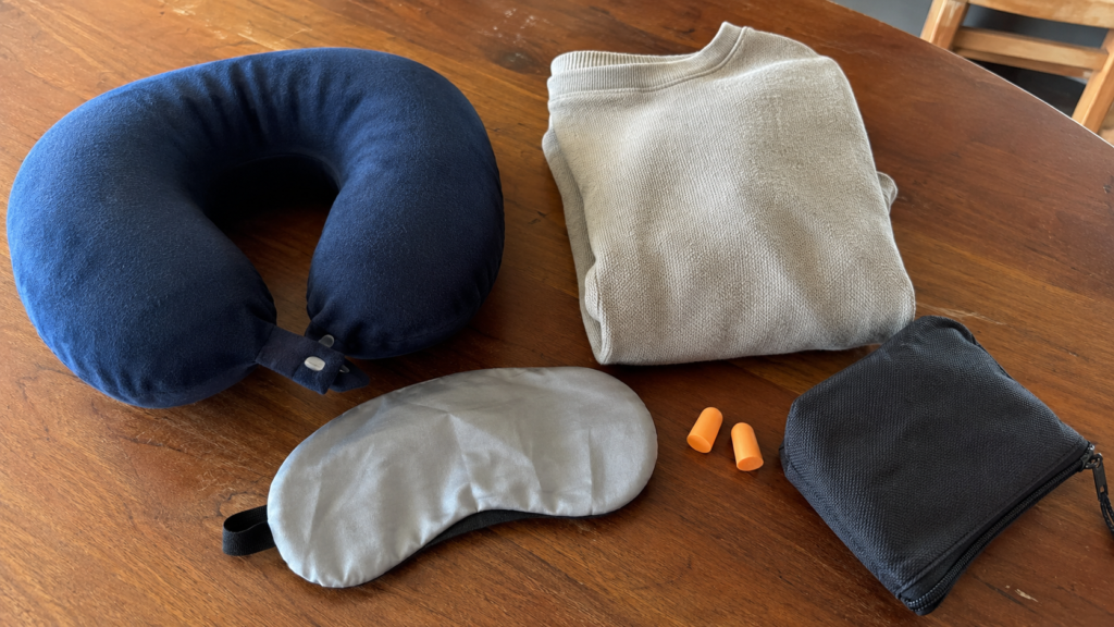 Night bus sleep kit laid out on a table: neck pillow, eye mask, earplugs and a light jumper
