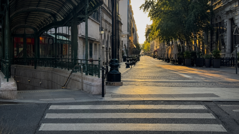 Pedestrian crossing at a city junction with a tram stop on one side and a walking street on the other