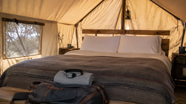 Packed essentials for a budget glamping trip laid on a tent bed