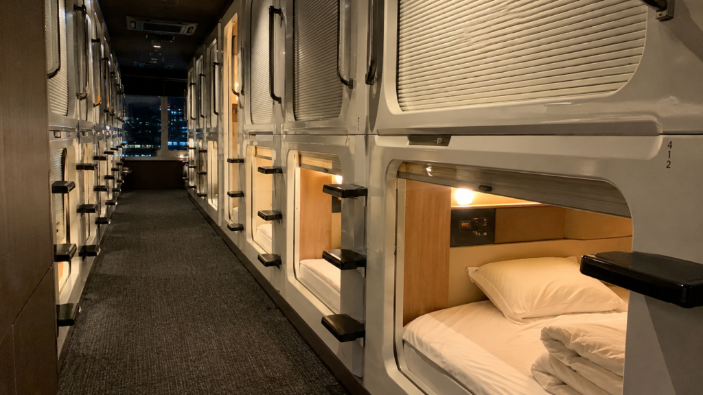 Rows of white capsule hotel pods with warm lighting in a Tokyo capsule hotel corridor